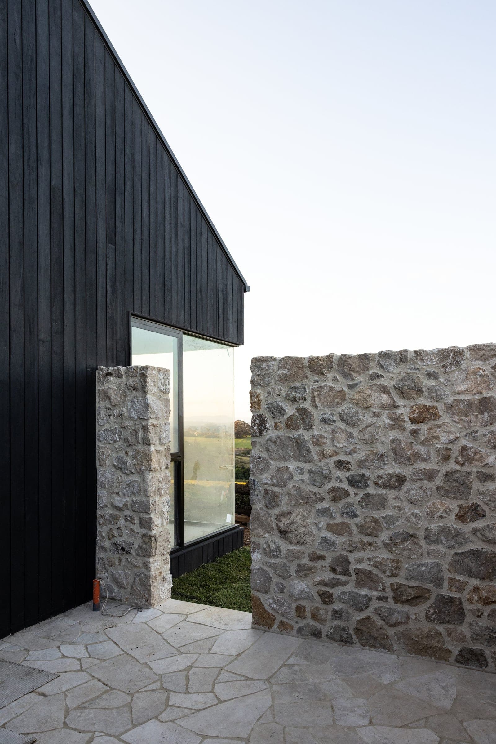 Charred timber cladding meeting a dry-stone wall at the Halls Road entry